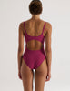 Person wearing a purple Araks swimsuit with cut-out design on a white background