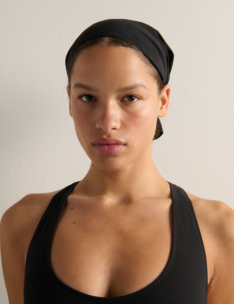 Person wearing a black swim cap and black bathing suit against a plain background