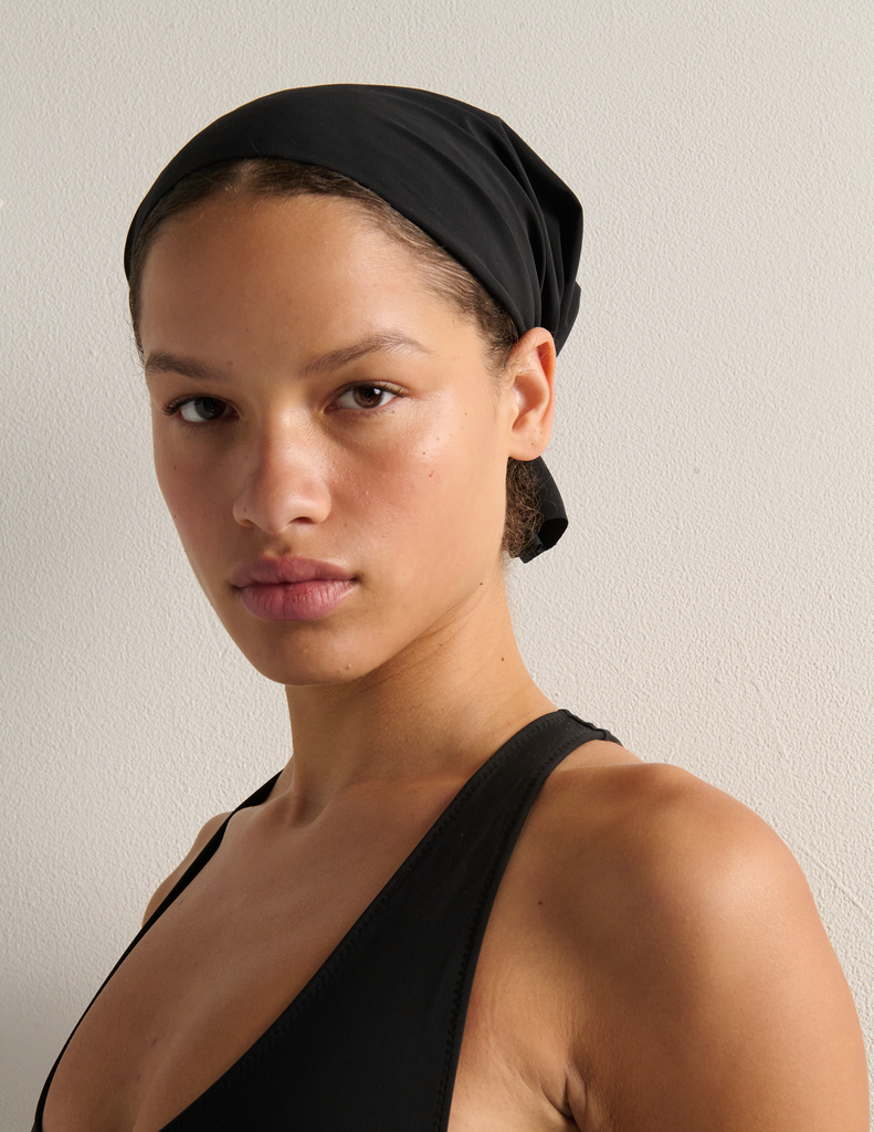 Person wearing a black swim cap and black bathing suit against a plain background