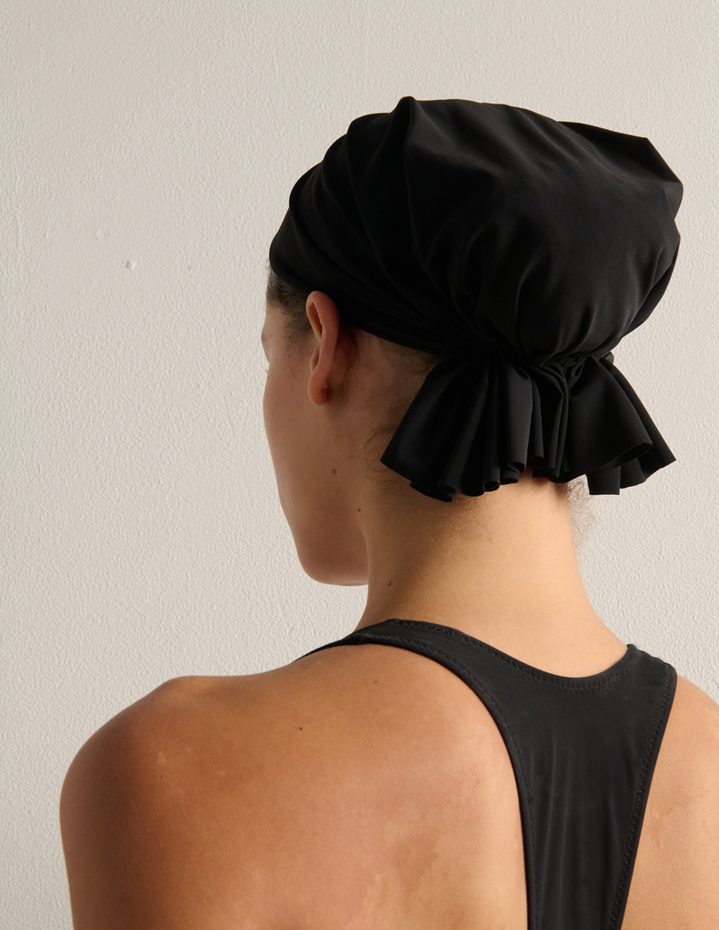 Person wearing a black swim cap and black bathing suit against a plain background