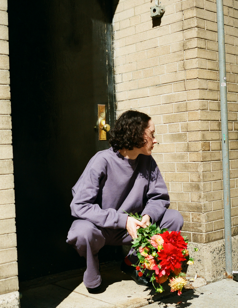A model posting outside a doorway while wearing the Araks Vivienne Crewneck in the shade Violette and the matching Vero sweatpants. 