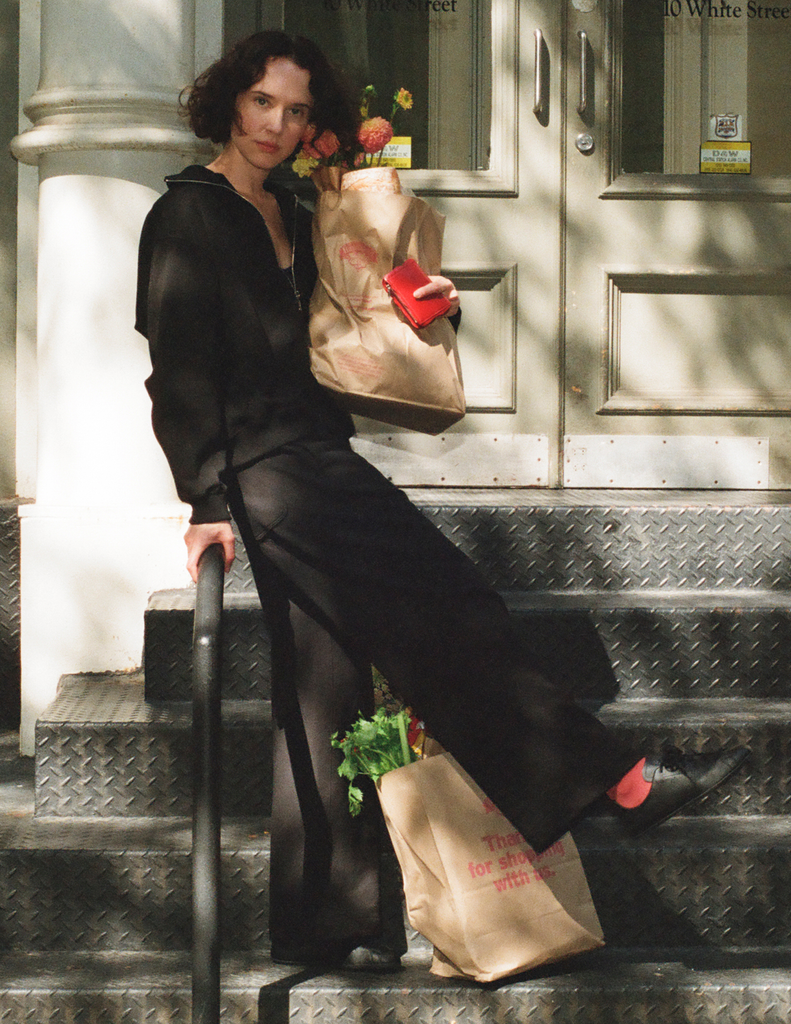A model wearing the Araks Vivienne and Vero sweatpants in black while posing on a staircase outside with flowers. 
