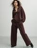 A model wearing the Araks matching dark brown lounge set, the Vivienne sweatshirt, and Vero sweatpants, both in the dark brown shade Mill. 