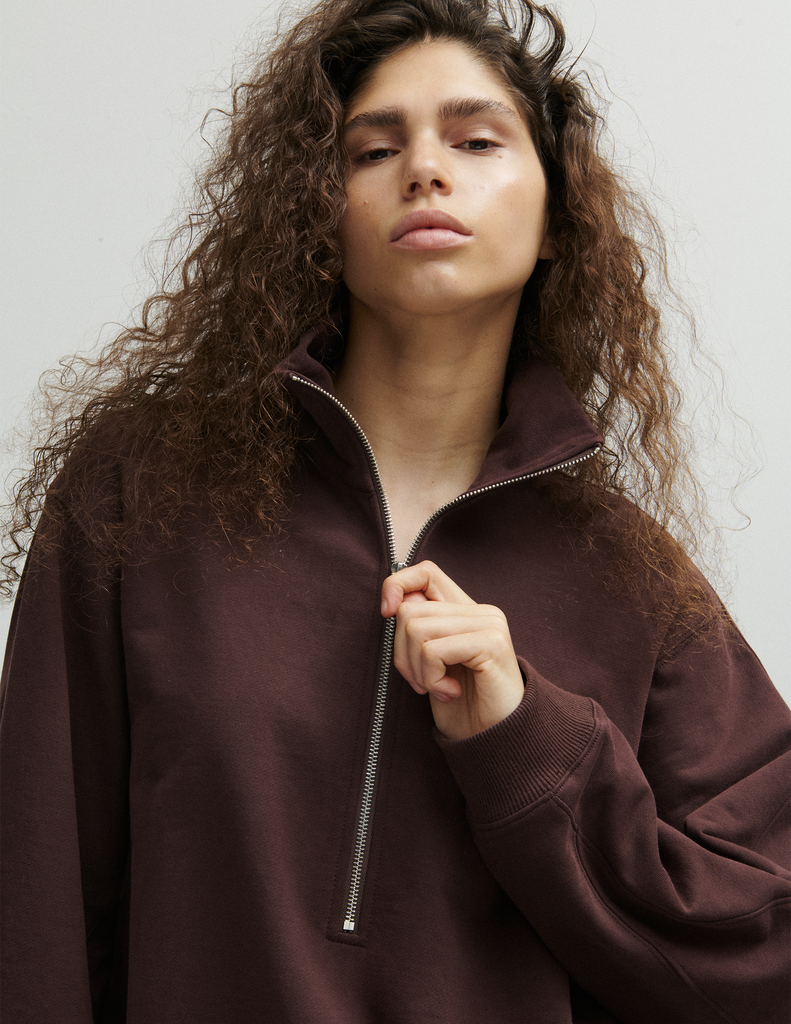 A model wearing the Araks matching dark brown lounge set, the Vivienne sweatshirt, and Vero sweatpants, both in the dark brown shade Mill. 