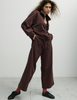 A model wearing the Araks matching dark brown lounge set, the Vivienne sweatshirt, and Vero sweatpants, both in the dark brown shade Mill. 