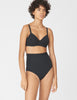 A model wearing a two-piece black swimsuit, consisting of a bralette-style bikini top with underwire and high-waisted bikini bottoms, against a light gray studio background.