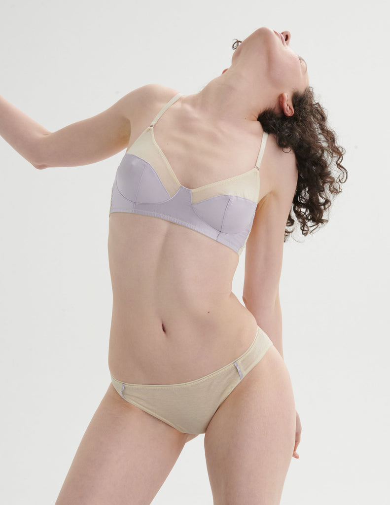 Woman wearing an araks cotton lavender bra and cream underwear on a plain background