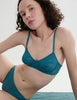 Woman wearing an Araks lace teal bralette and panties set against a white background