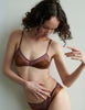 Woman wearing an Araks brown silk bralette  and panties set against a plain background