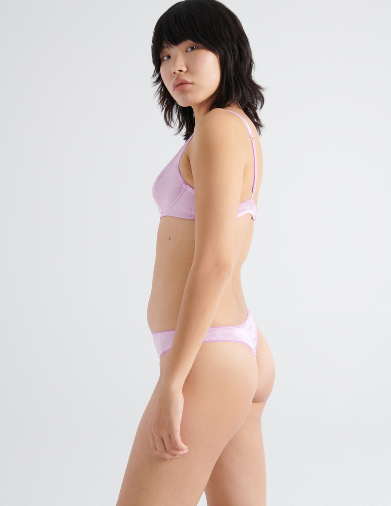 Profile view of model wearing pink silk thong with matching underwire bra. 
