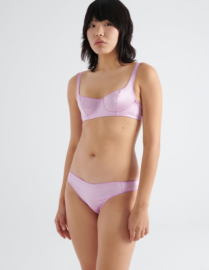 Three quarter view of model wearing pink silk underwire bra with matching silk panties. 