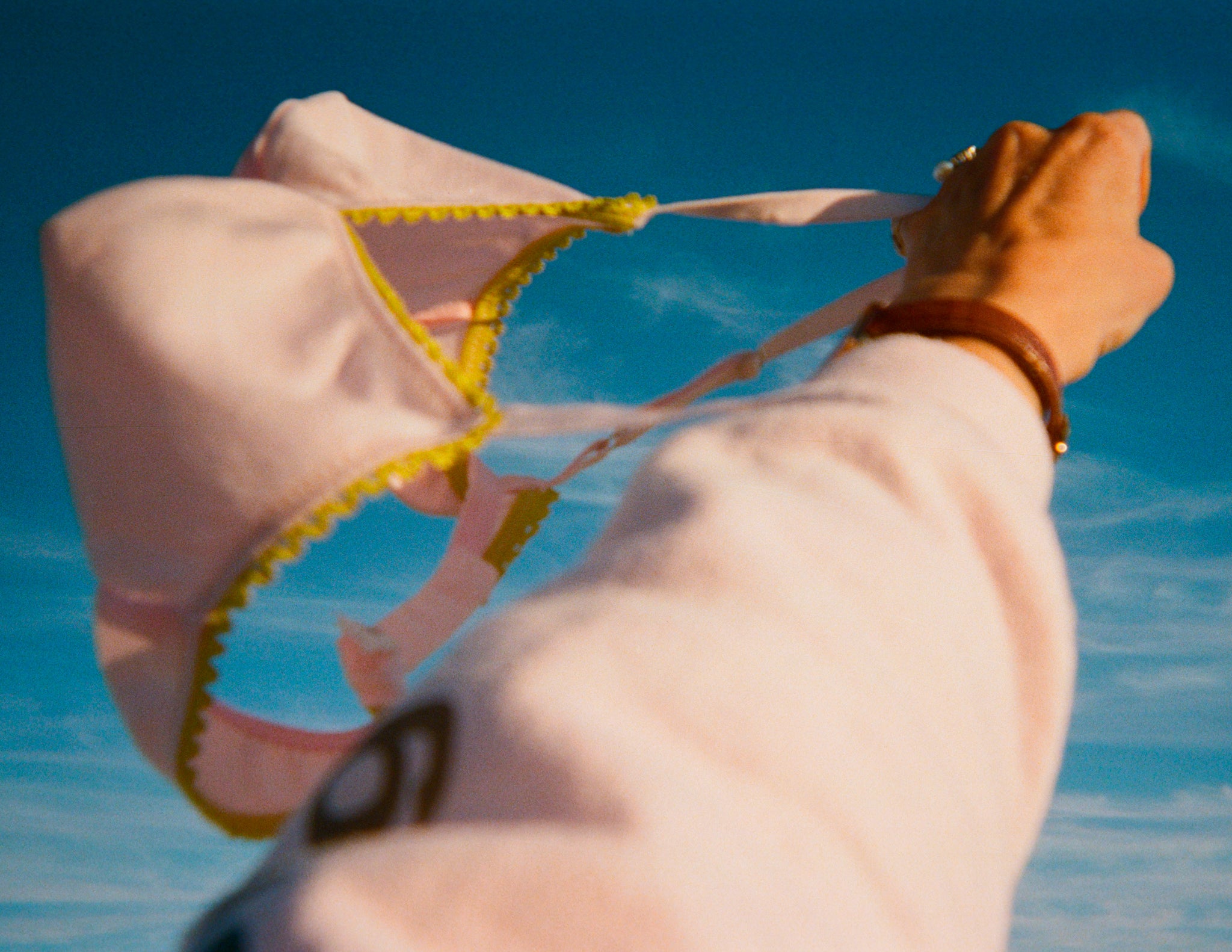 Person holding a pink bikini top with yellow trim against a blue sky.