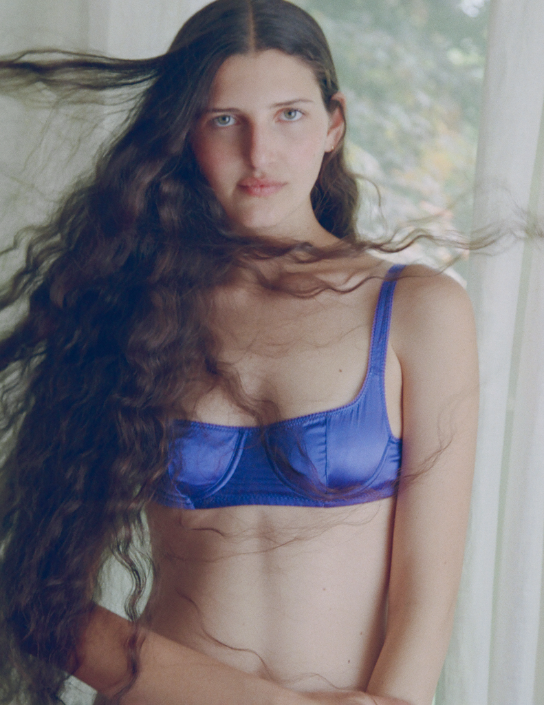 Woman wearing an Araks silk underwire blue bra with long hair blowing in the wind.