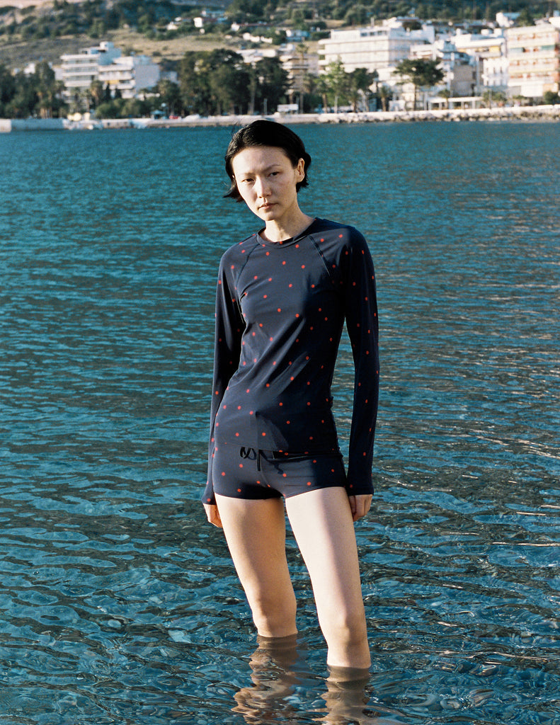 Model wearing Araks Undine rashguard with Polly swim shorts in navy with red polka dots