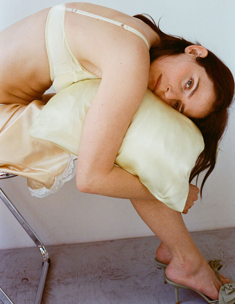 Woman holding a pillow against a plain background, while wearing penelope bralette in butter