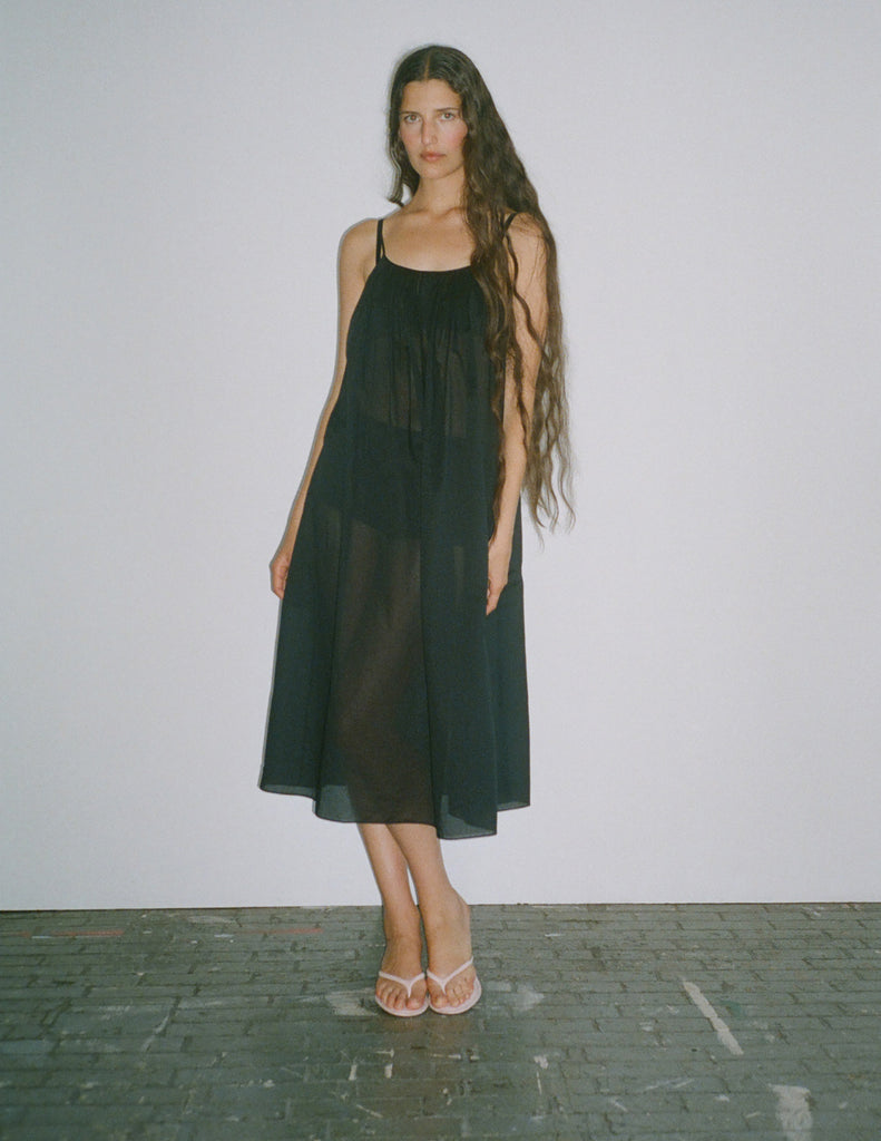 A model standing against a white backdrop, while wearing a rafaella slip dress in black. 