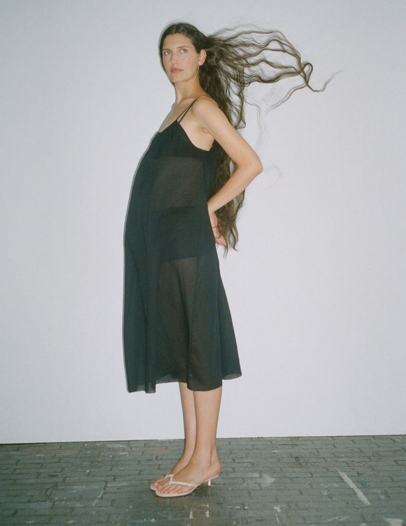 A model standing against a white backdrop, while wearing a rafaella slip dress in black. 