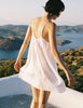 A model standing by a body of water and mountains, while wearing a white Sarra slip dress from Araks