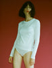 Person wearing an Araks 100% Organic Cotton white long-sleeve tee with white panties against a red background