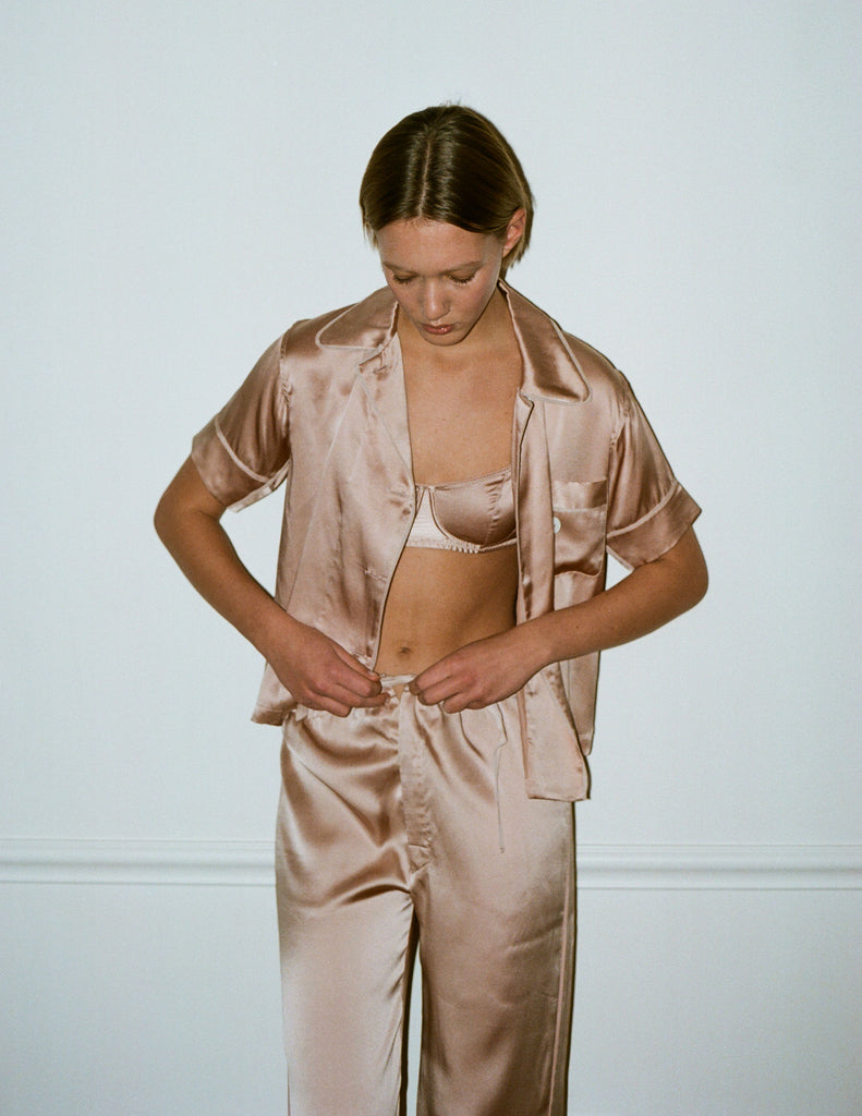 Woman wearing an Araks silk pajama set against a plain background