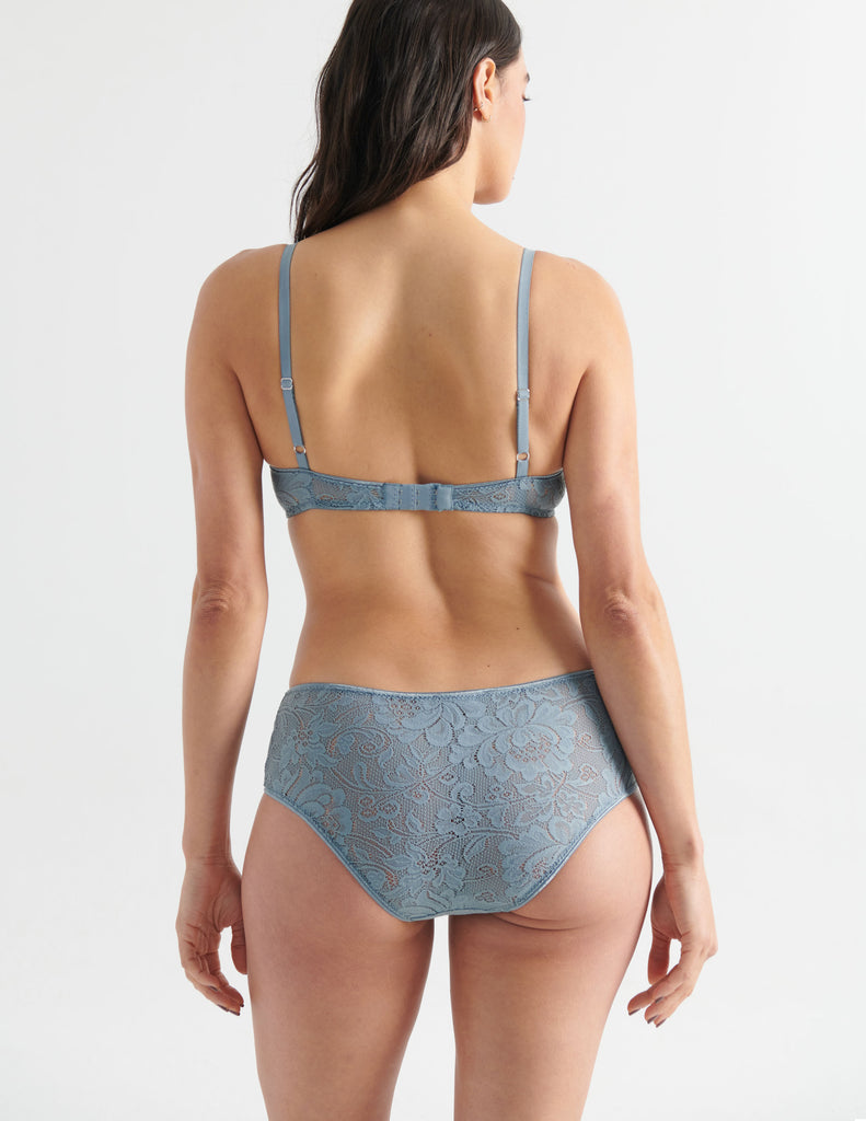 Back view image of model wearing grey lace hipster panties with matching bralette. 