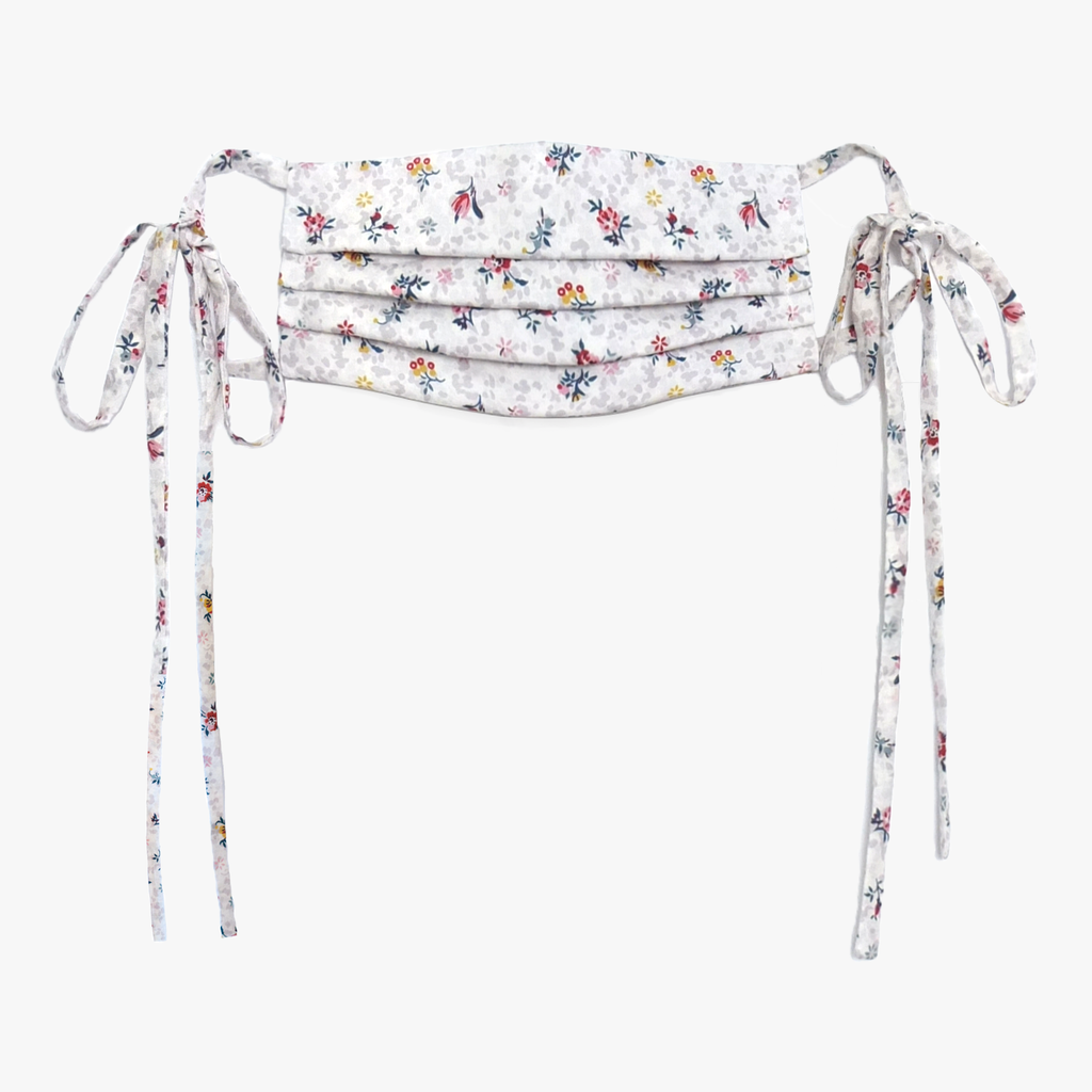 Cotton face mask made from printed fabric. The design is white with red and yellow flowers. The mask ties on each side.