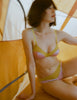Woman in a yellow and pink bralette and matching panty  sitting under a yellow tent.