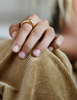 Image of woman's hand resting on her knee wearing solid 18k yellow large gold dome ring for weddings and milestones. Soft curves. Heavy. Not hollow.