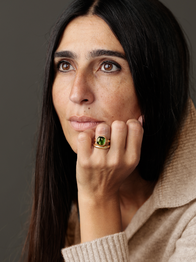 Hand with gold ring with a green gem on woman's face.