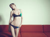 Model near a couch, wearing a black and green asymmetrical bralette and matching panty