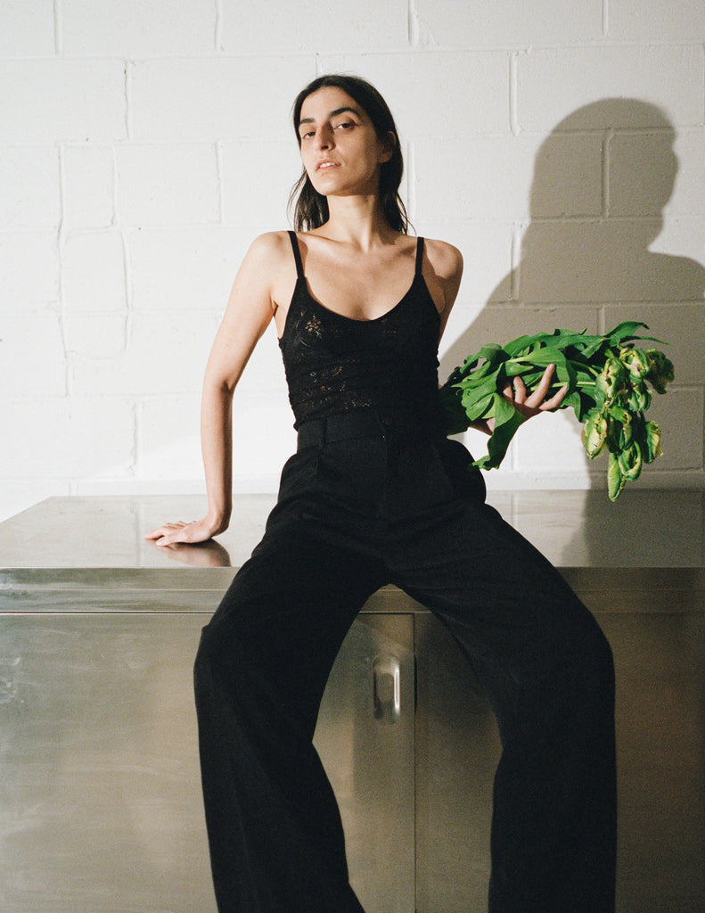 Editorial style image of model wearing black lace tank and black trousers holding a bundle of green