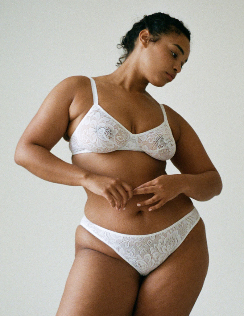 Woman wearing white, lace wireless bralette with matching straps, and matching panty