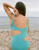 Back of woman sitting at beach with blue cut out one piece.