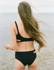 Back of woman in black bikini with cutouts at beach.