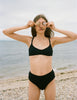 Woman at beach wearing black rib bikini top with matching bottom with shells over eyes