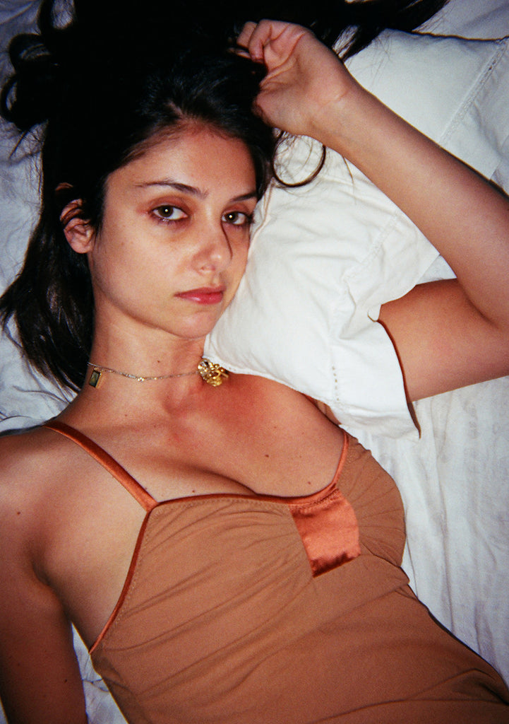 Woman on bed, wearing light orange with a orange panel top
