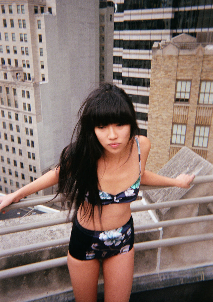 Woman outside in front of buildings wearing black based floral bralette with matching high waisted bottoms.