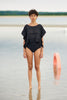woman on beach wearing black ruffle top and black bikini bottoms.