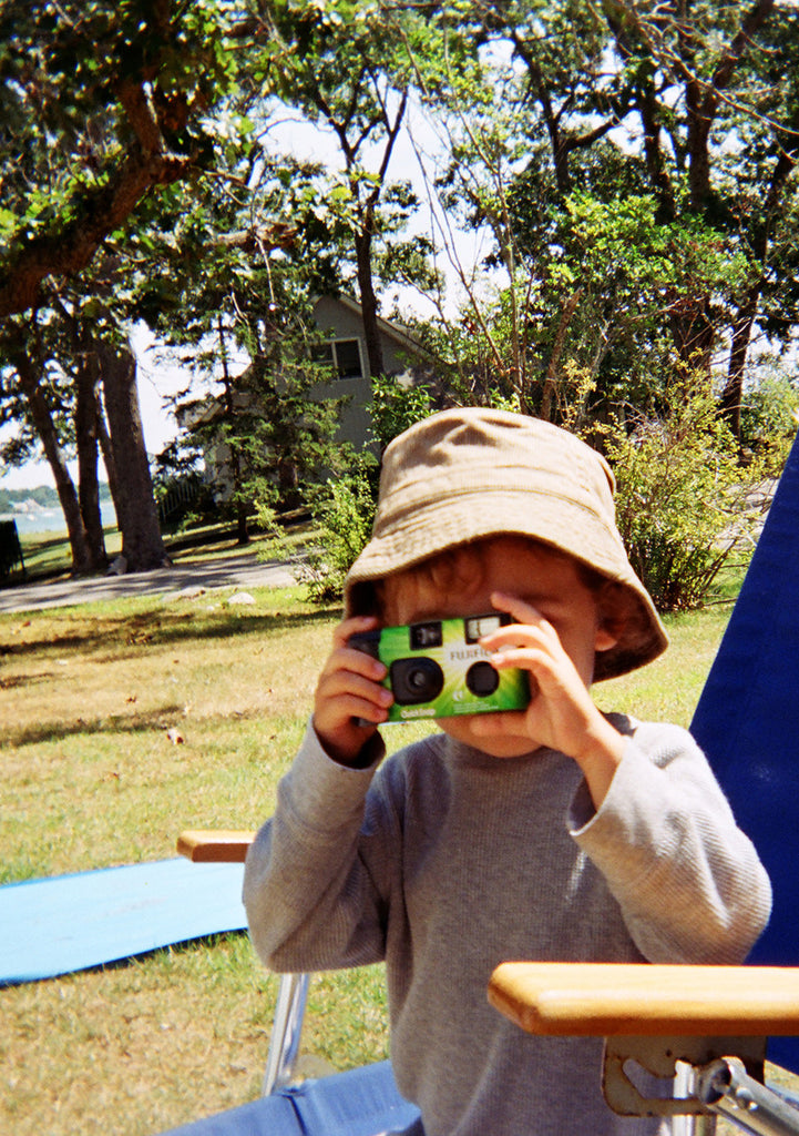 Boy outside taking photo with disposable camera.