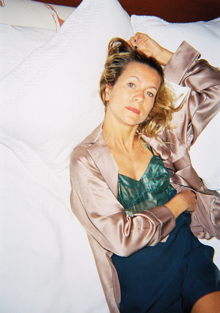 Woman on bed, wearing pale pink sleep shirt, and a green and blue slip