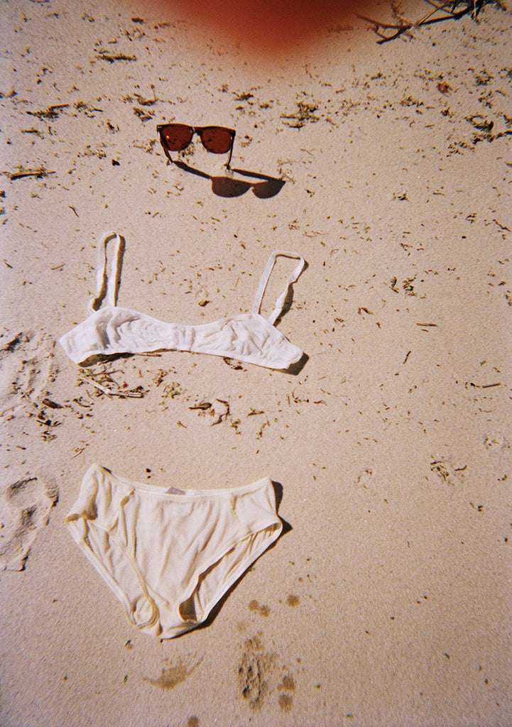 On sand with sunglasses, white bralette and light nude panty.
