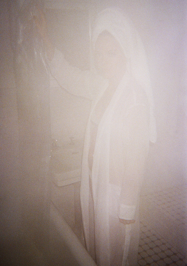 Woman in bathroom wearing white silk robe.