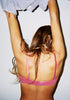 Back shot of woman with arms above her head, taking off a t-shirt underneath wearing pink silk chiffon wireless bralette with dark pink silk charmeuse. 