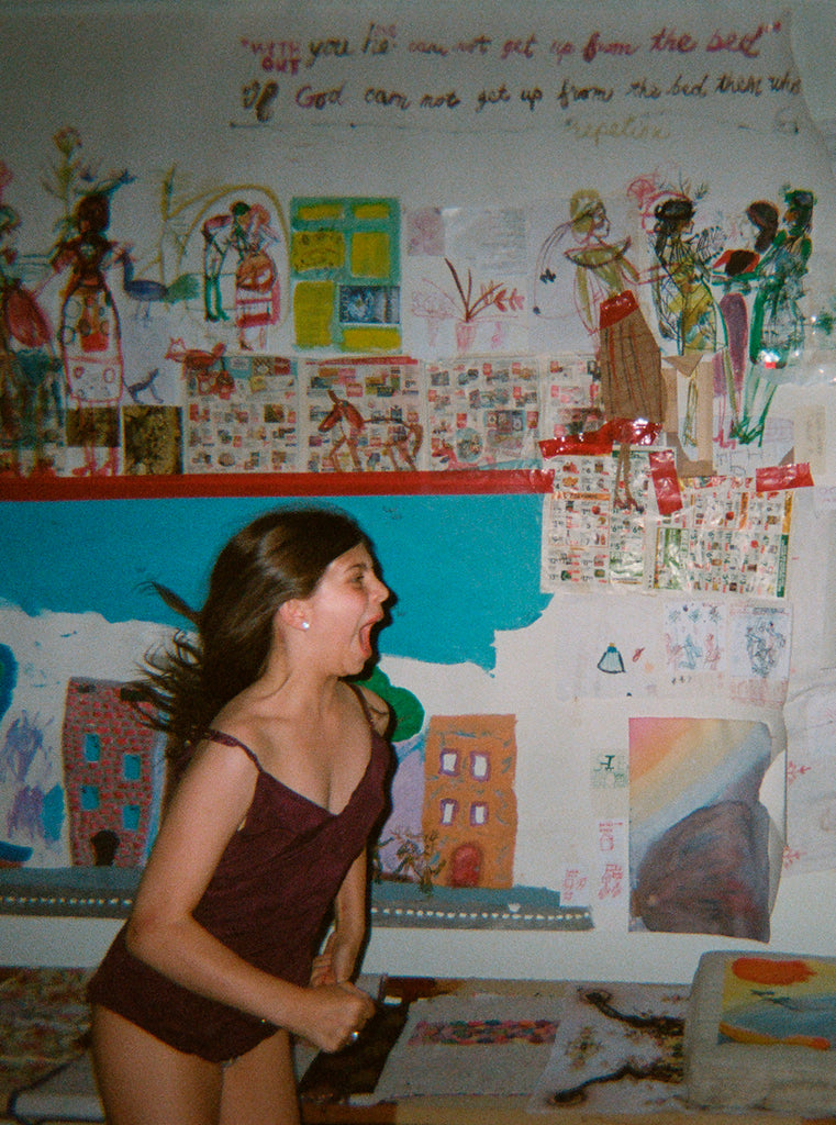 Model in a room with artwork, wearing a maroon bodysuit