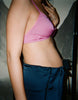 Model's side, wearing pink bralette with light pink trim, and navy pants