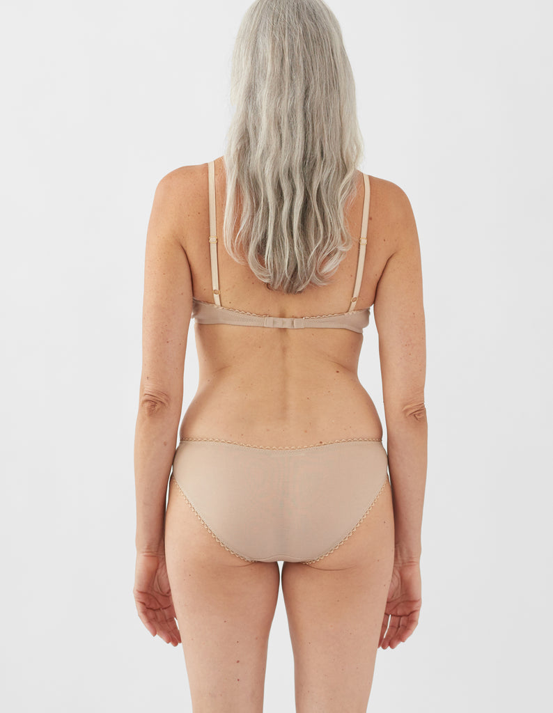Back view of a woman wearing nude bralette with nude trim and matching panty.