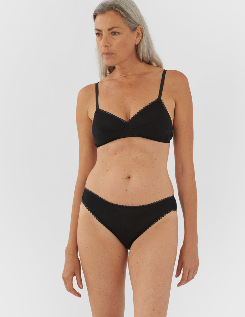 Front view of woman wearing black panty with white trim, and matching bralette.