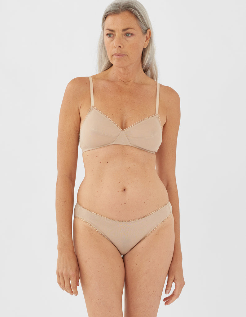 Front view of a woman wearing nude araks organic cotton bralette with nude trim and matching panty.