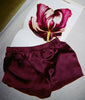 Burgundy silk charmeuse pajama shorts with elastic band draped over a flower and open book.