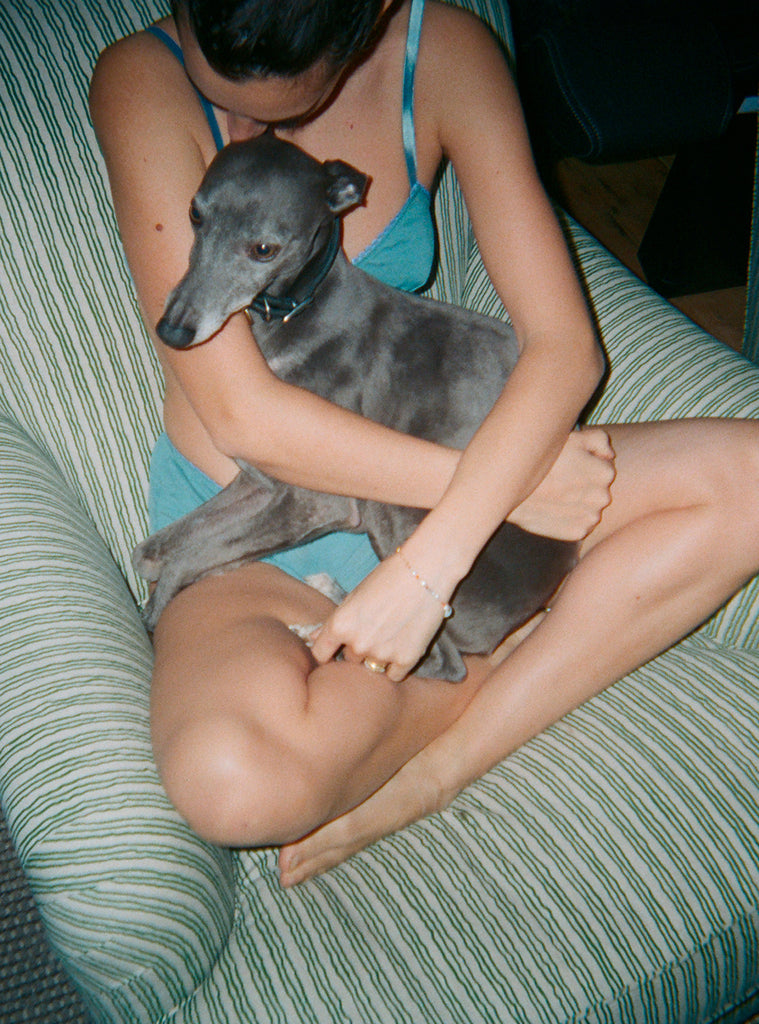 Woman sits holding dog, wears turquoise bra with turquoise shiny straps, and matching panty
